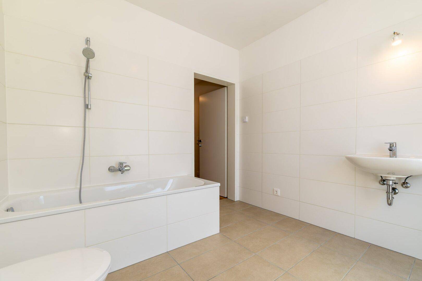 Helles Badezimmer mit Badewanne, Waschbecken und weißen Wandfliesen, in neuwertigem Zustand.