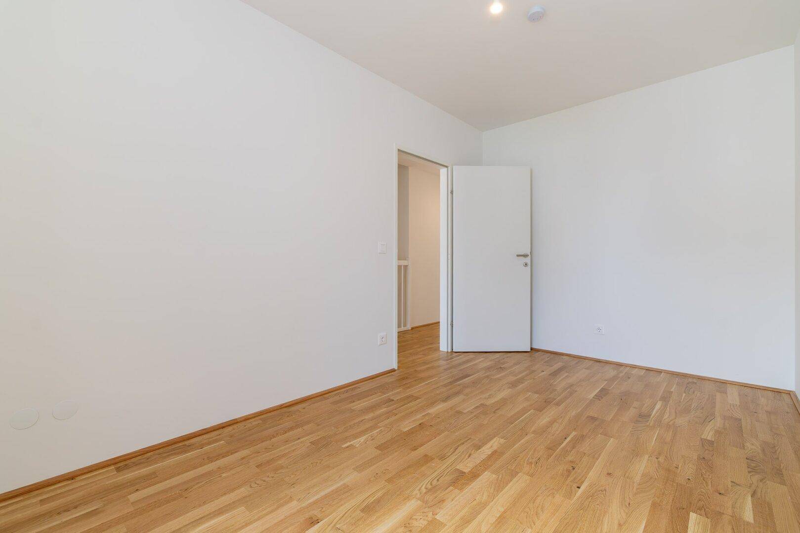 Leeres Zimmer mit hellem Parkettboden und weiß gestrichenen Wänden, bereit zur individuellen Gestaltung.