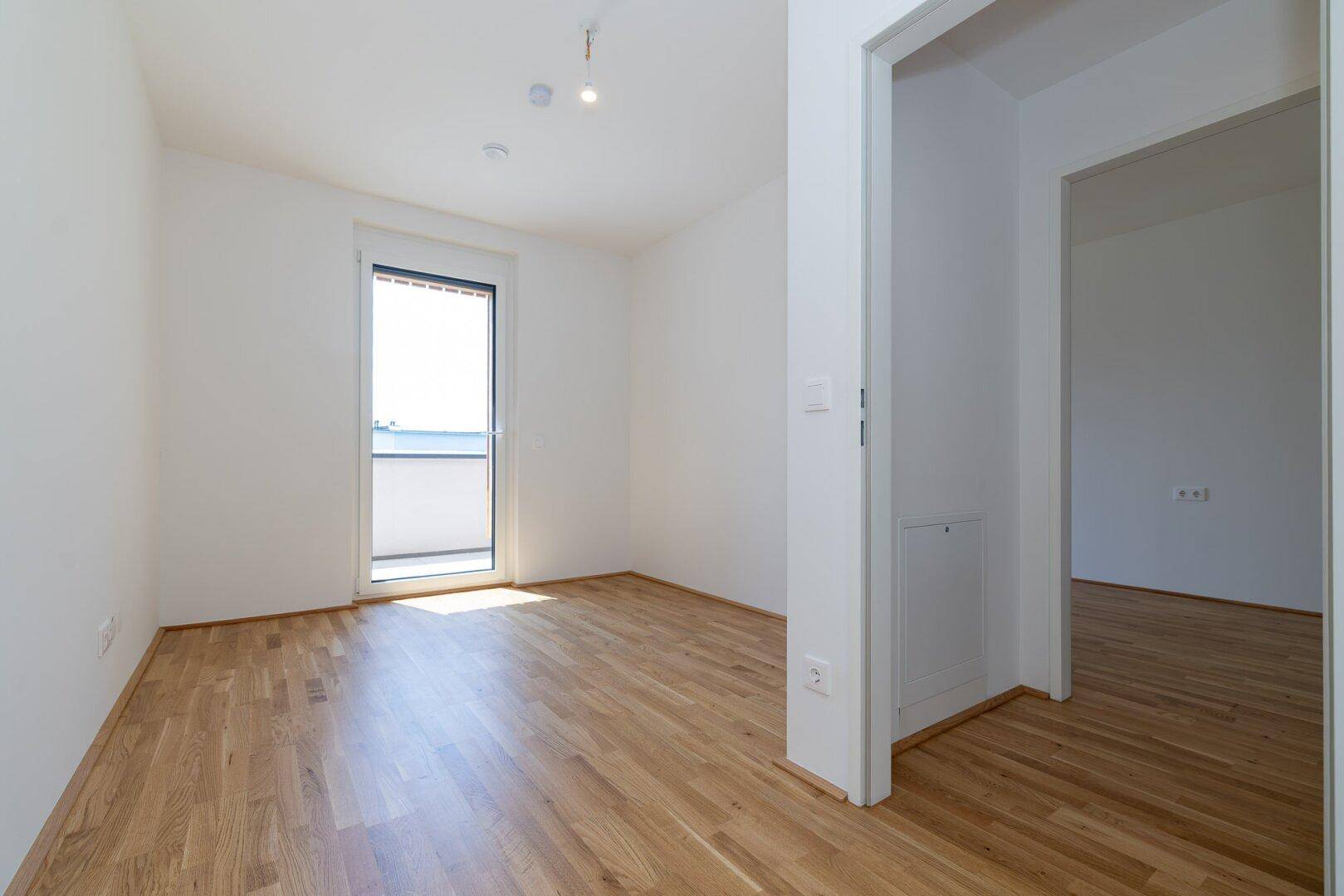 Helles Schlafzimmer mit Parkettboden und Zugang zu einem kleinen Balkon, ideal für frische Luft.