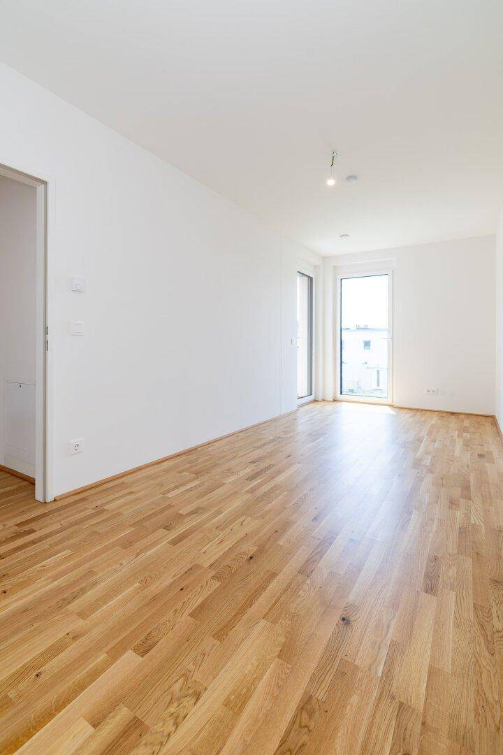 Geräumiges, unmöbliertes Zimmer mit Parkettboden und großen Fenstern für viel Tageslicht.
