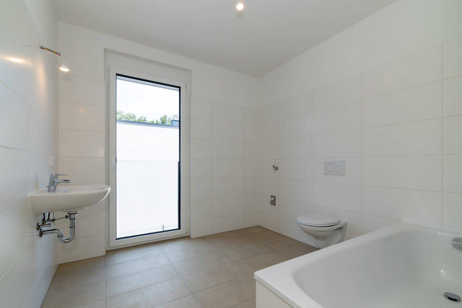 Modernes Badezimmer mit Badewanne, Waschbecken, WC und Fenster für natürliche Belüftung.