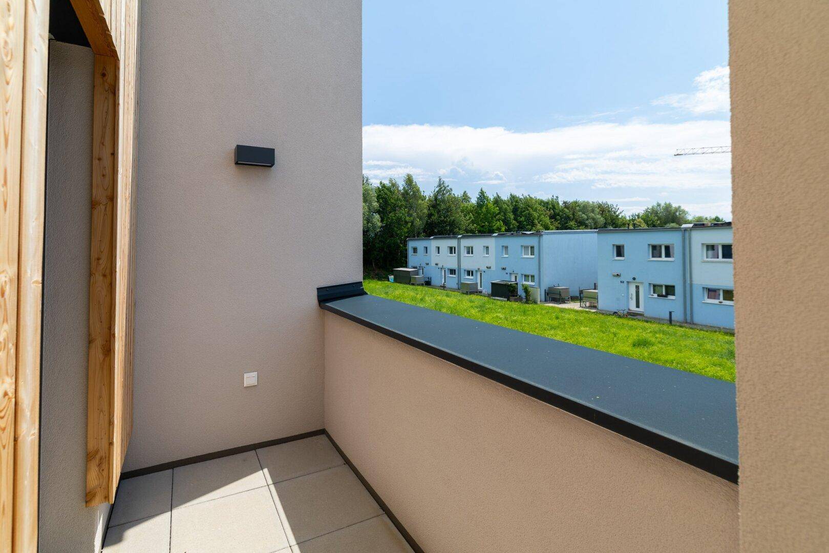 Kleiner Balkon mit Fliesenboden und Blick auf die grüne Umgebung und benachbarte Häuser.