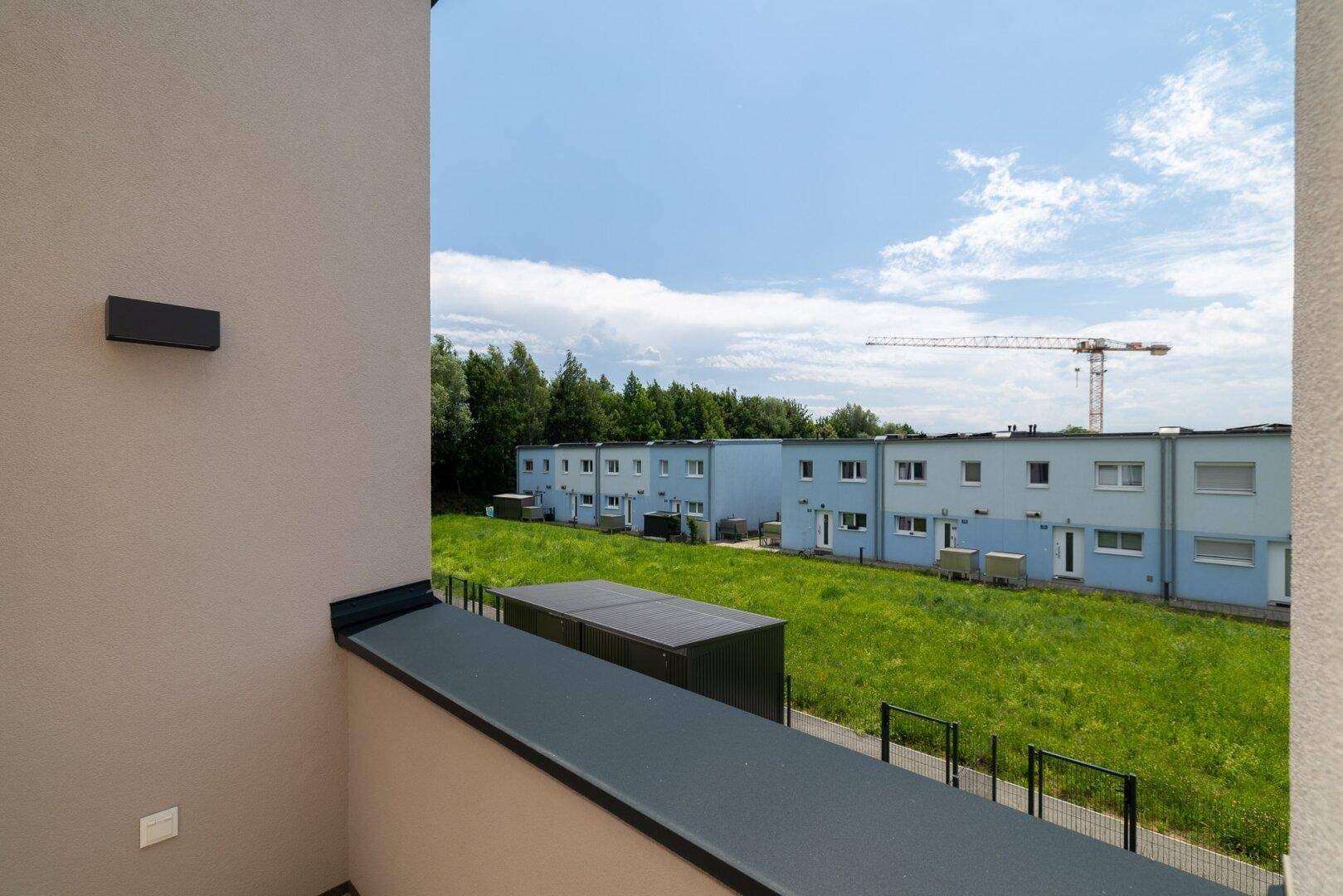 Balkon mit Blick auf die Nachbarschaft und einen Kran am Horizont, umgeben von viel Grün.