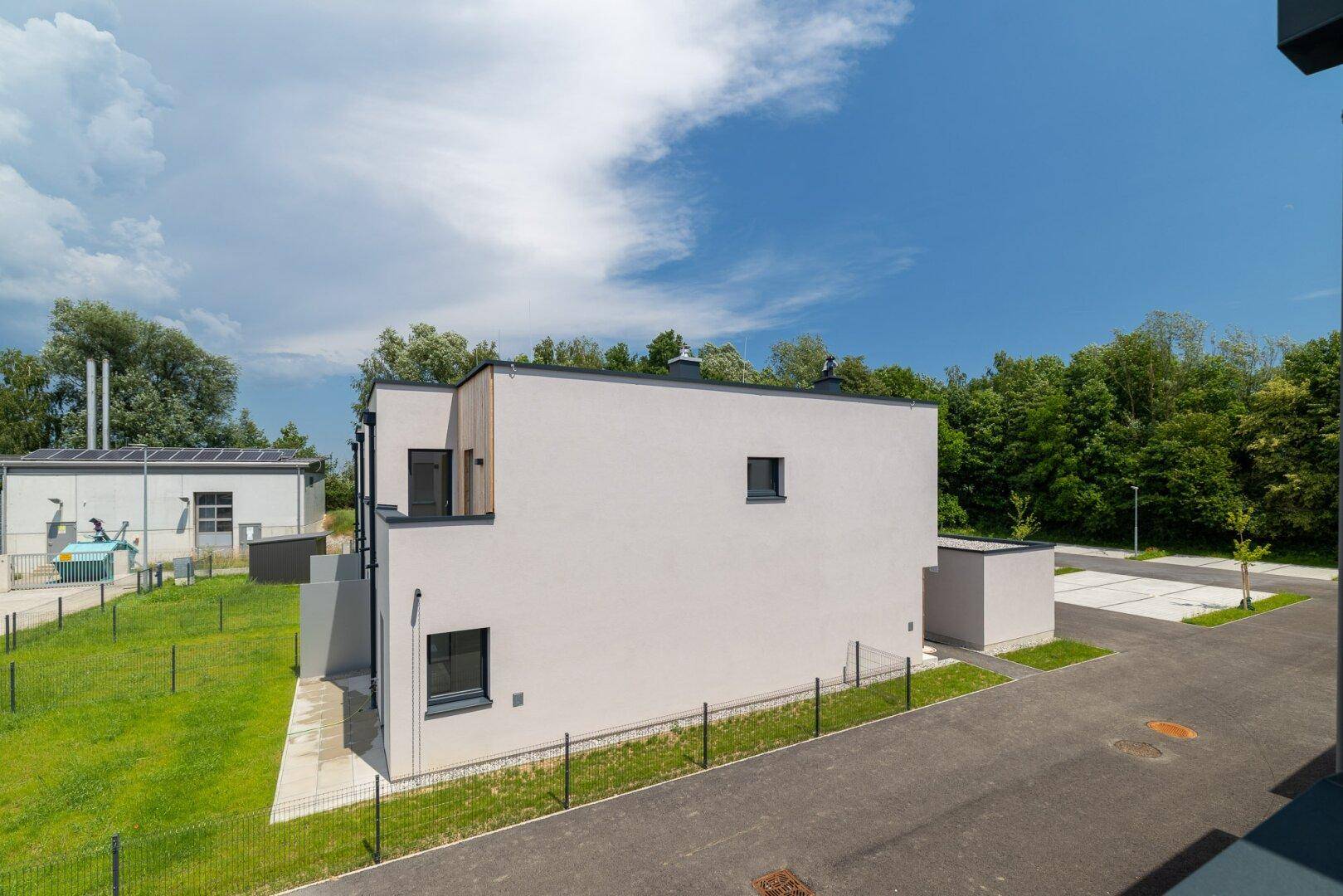Moderne Reihenhausfassade mit klaren Linien und großen Fenstern, umgeben von Grünflächen.