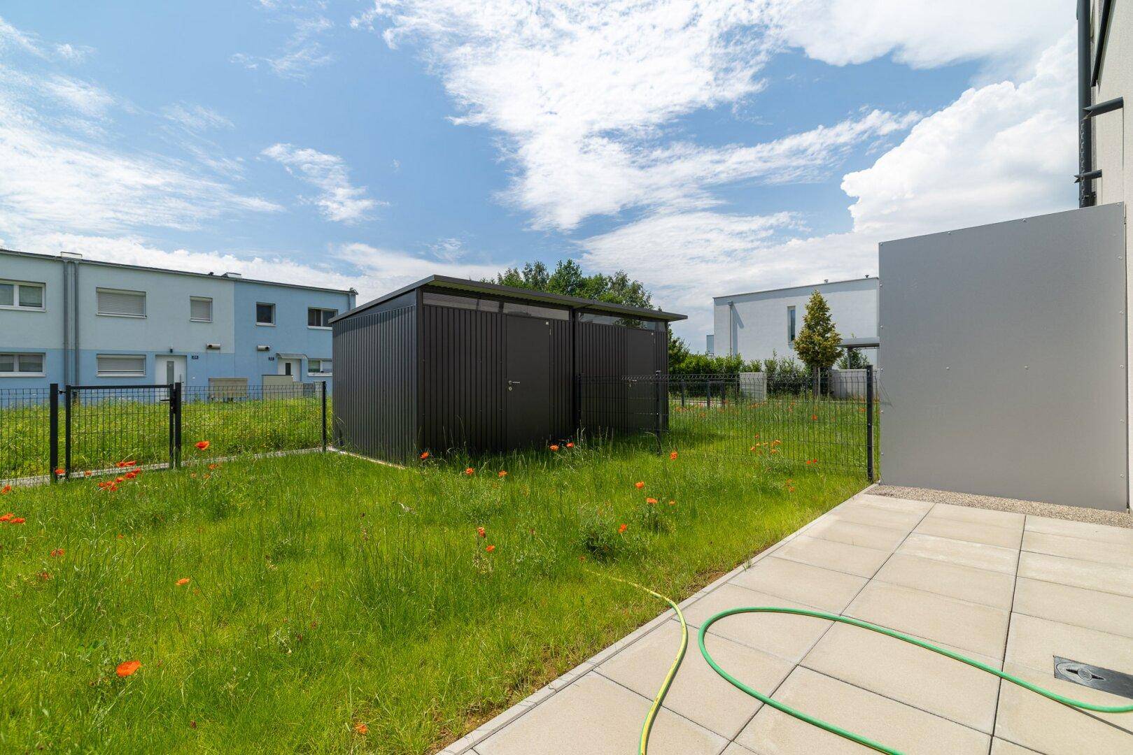 Sonniger Garten mit Rasen, gepflastertem Terrassenbereich und Blick auf die Umgebung.