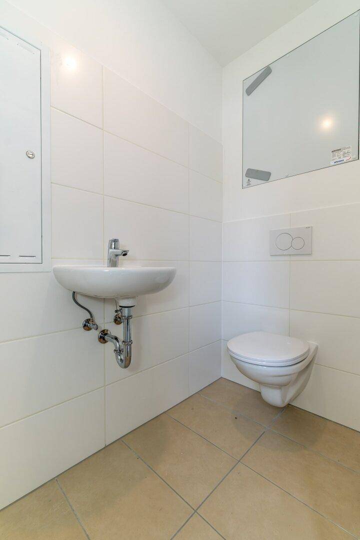 Kleines Gäste-WC mit weißen Fliesen, wandhängendem WC und Waschbecken.