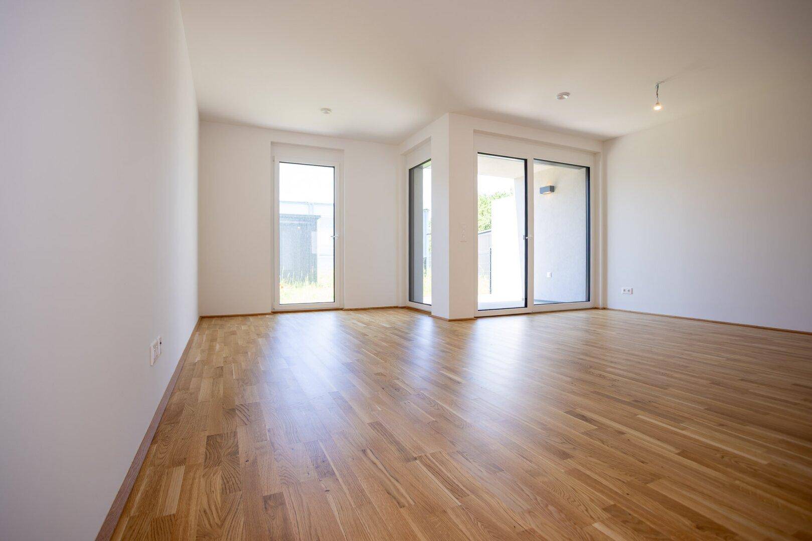 Lichtdurchfluteter Wohnbereich mit Holzboden und großen Fenstern, die viel Tageslicht hereinlassen.