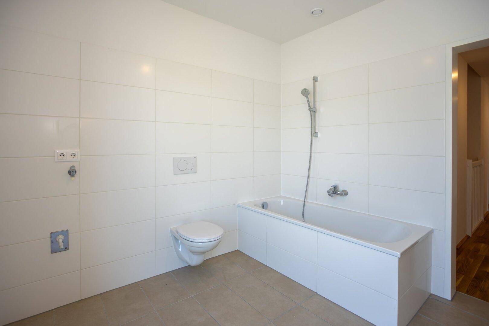 Modernes Badezimmer mit weißen Fliesen, Badewanne und wandhängendem WC.