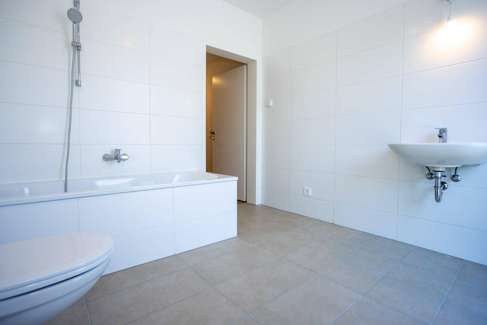 Geräumiges Badezimmer mit Badewanne, Waschbecken und WC, alles in hellen Farben gehalten.