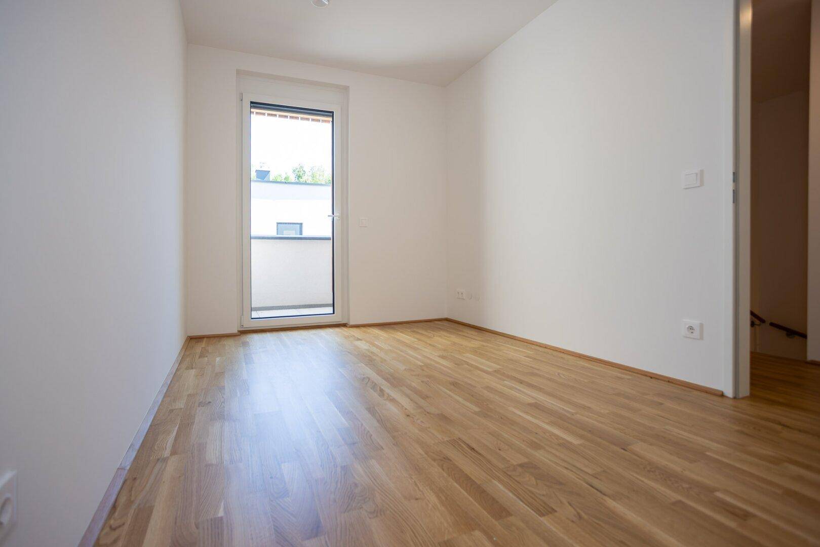 Helles Schlafzimmer mit Holzboden und Zugang zu einem kleinen Balkon, ideal für frische Luft.