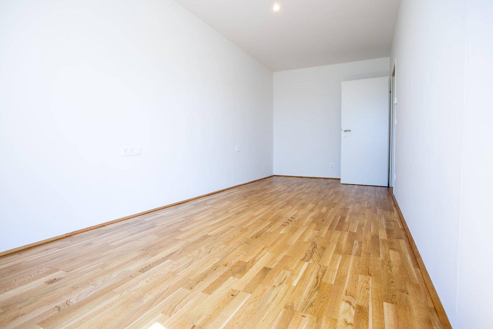 Leeres Zimmer mit hellem Holzboden und weißen Wänden, vielseitig nutzbar als Schlaf- oder Arbeitszimmer.