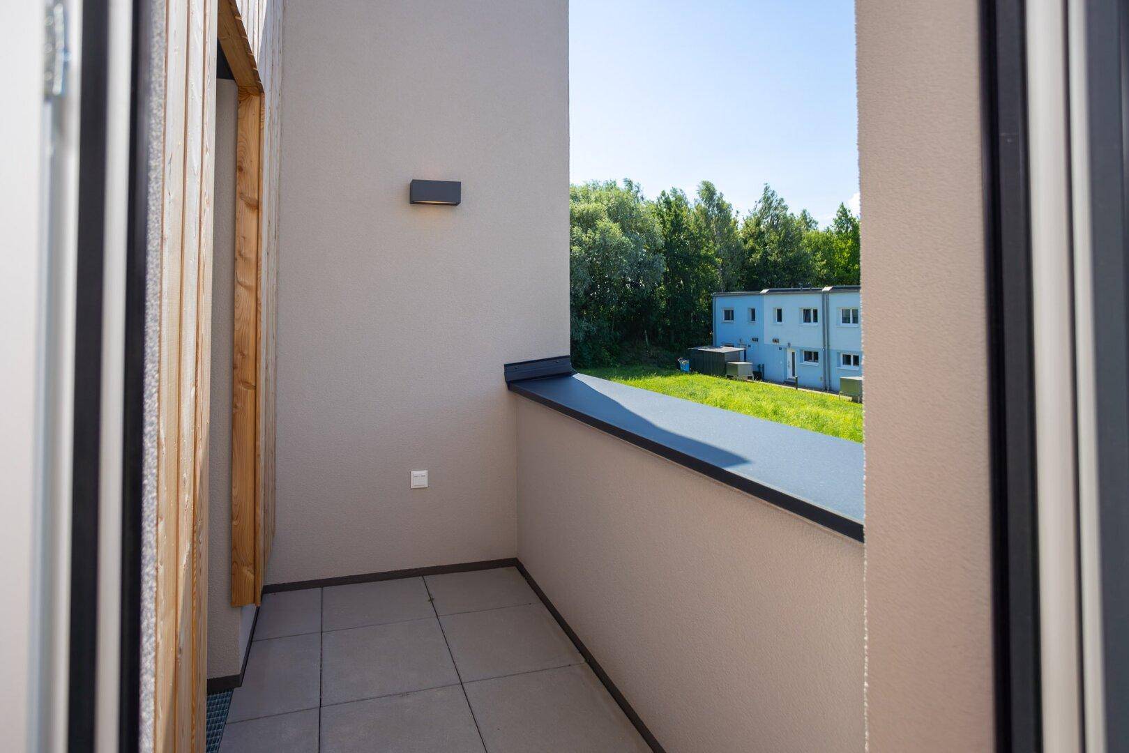 Kleiner Balkon mit Fliesenboden und Blick auf die umliegenden Gebäude und Bäume.