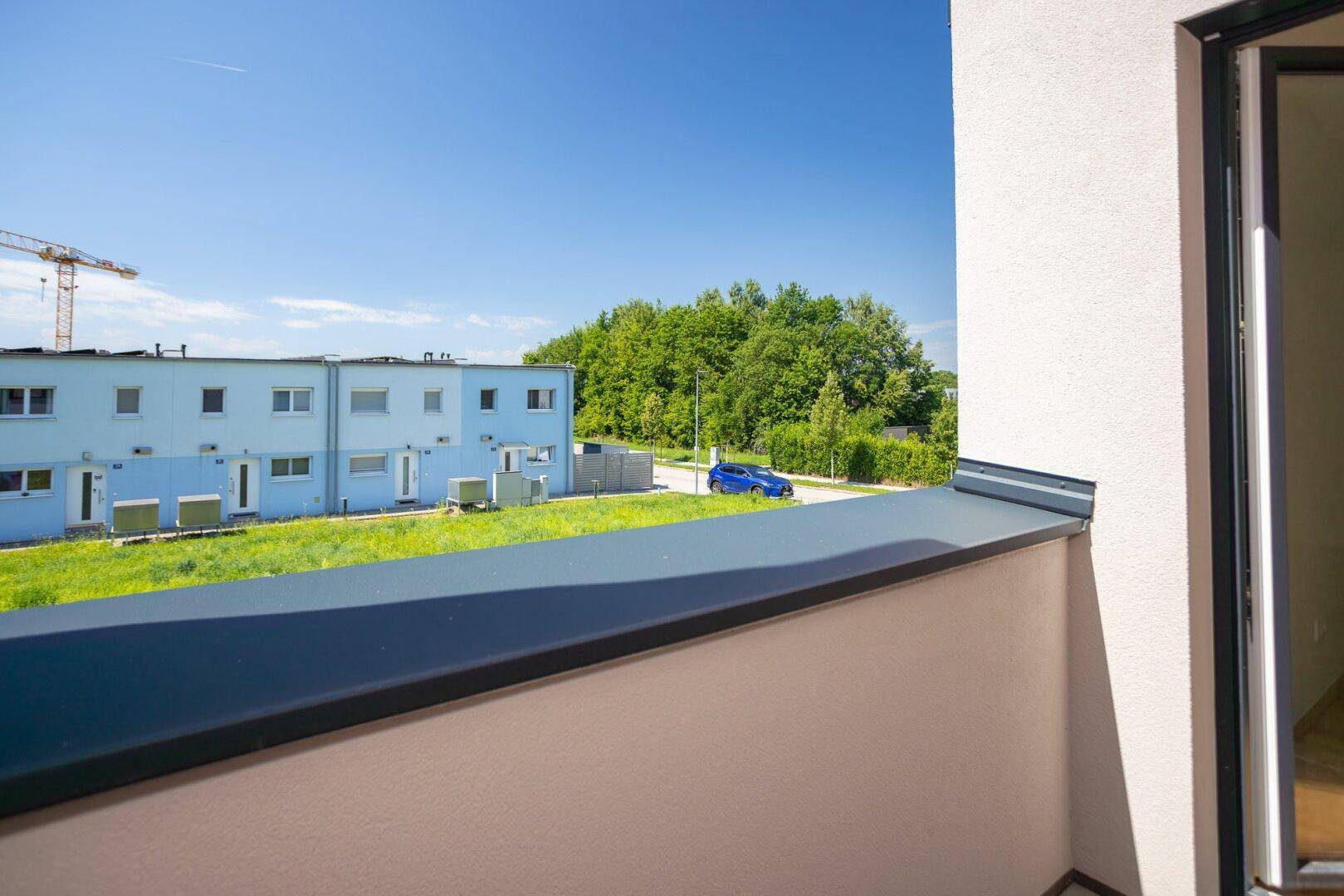 Blick vom Balkon auf die umliegenden Reihenhäuser und grüne Bäume unter blauem Himmel.