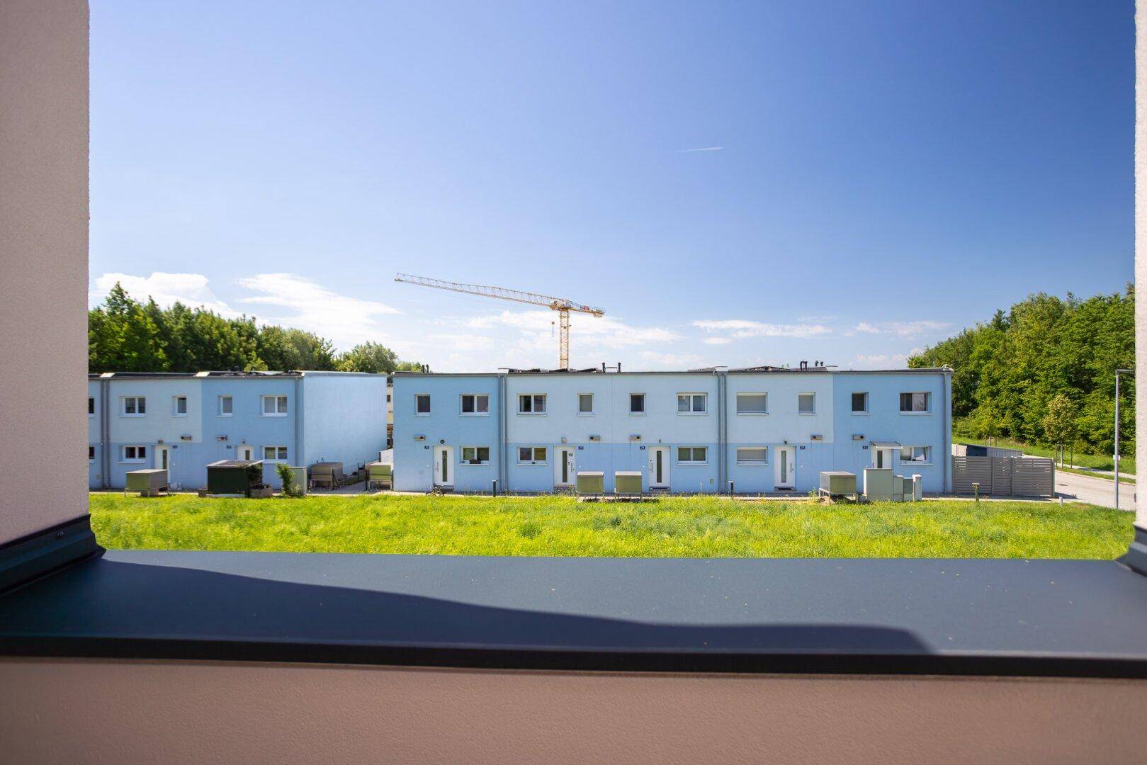 Weitblick aus dem Fenster auf die Nachbarhäuser und die grüne Umgebung an einem sonnigen Tag.