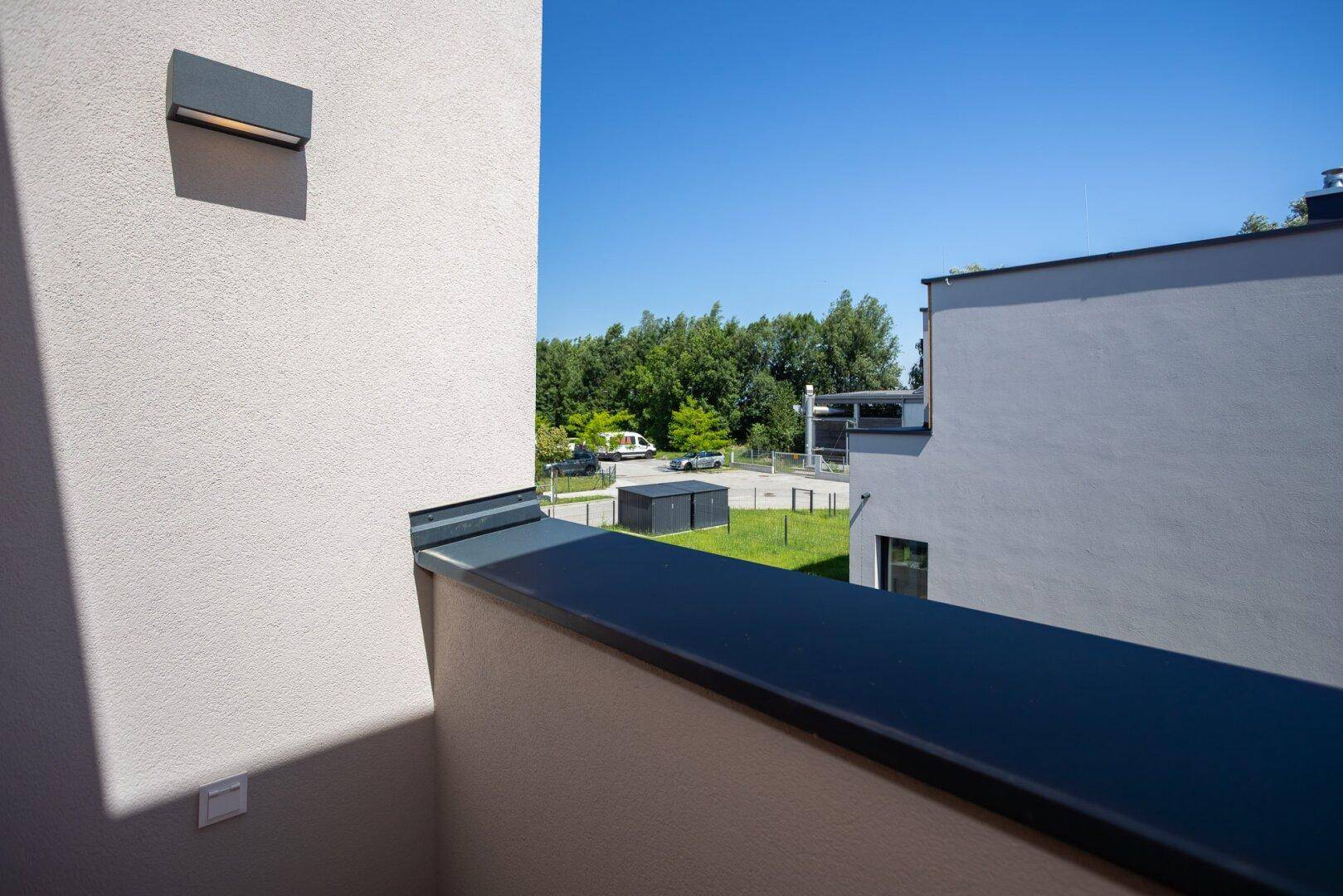 Balkon mit moderner Wandleuchte und Blick auf die grüne Umgebung und die Straße.