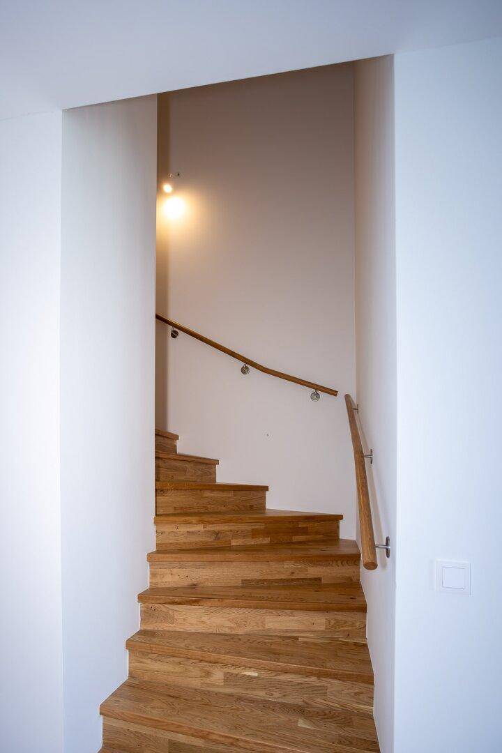 Helle Holztreppe mit modernem Geländer, die in die oberen Stockwerke führt.