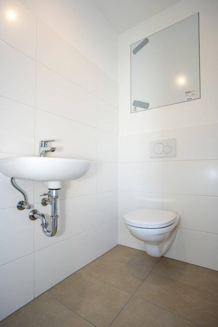 Kleines Gäste-WC mit weißen Fliesen, modernem Waschbecken und wandhängender Toilette.