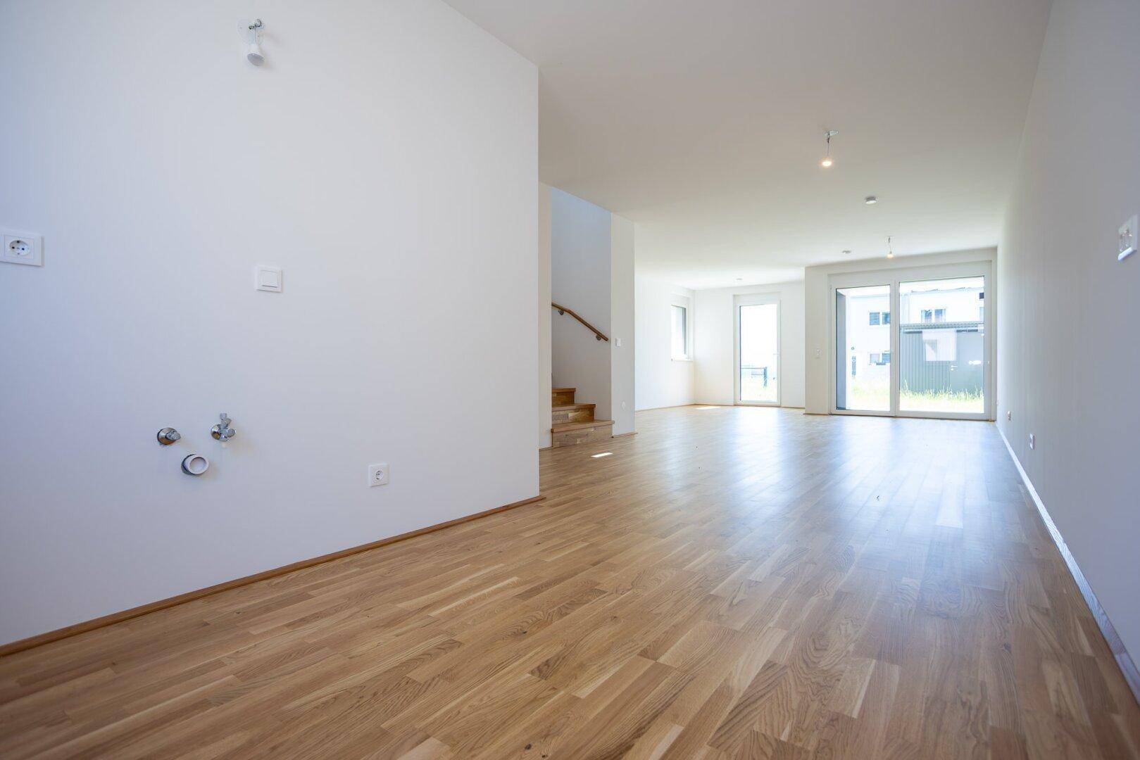 Geräumiger, heller Raum mit Eichenparkett, vorbereitet für eine moderne Küche und offenem Wohnbereich.