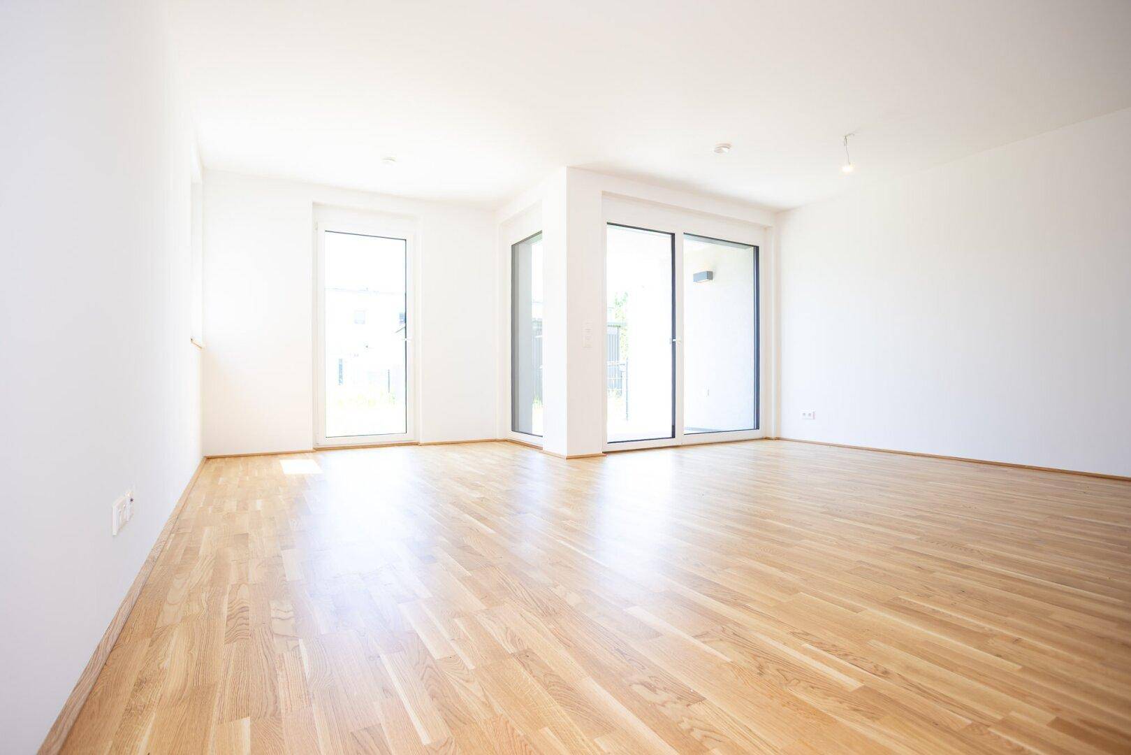 Helles, leeres Wohnzimmer mit Eichenparkettboden und großen Schiebetüren zur Terrasse.