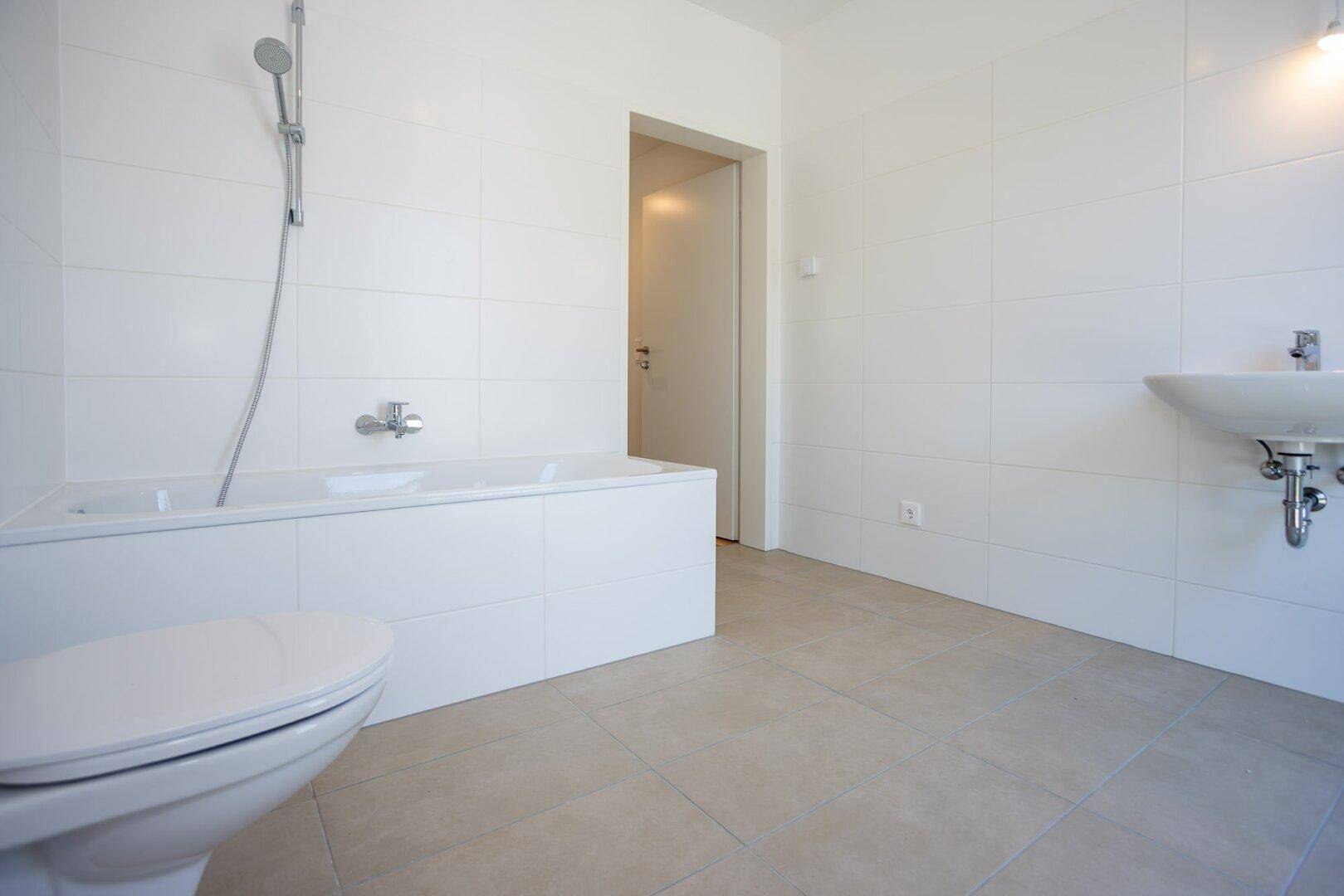 Modernes Badezimmer mit weißen Fliesen, Badewanne mit Duschfunktion und wandhängendem WC.