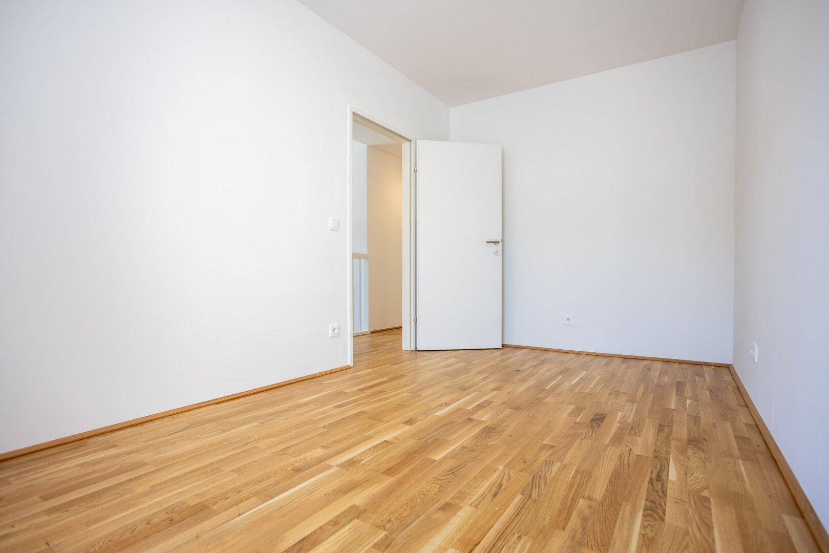 Leeres Schlafzimmer mit hellem Eichenparkettboden und weiß gestrichenen Wänden, bereit zum Einzug.