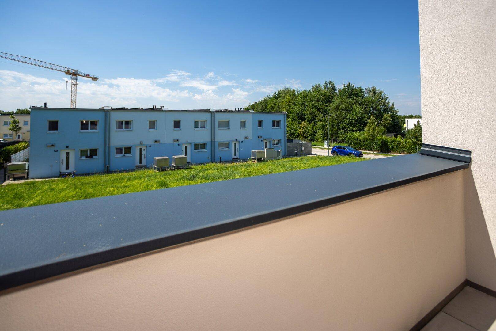 Blick vom Balkon auf eine grüne Umgebung mit weiteren Wohngebäuden und einem Baukran in der Ferne.