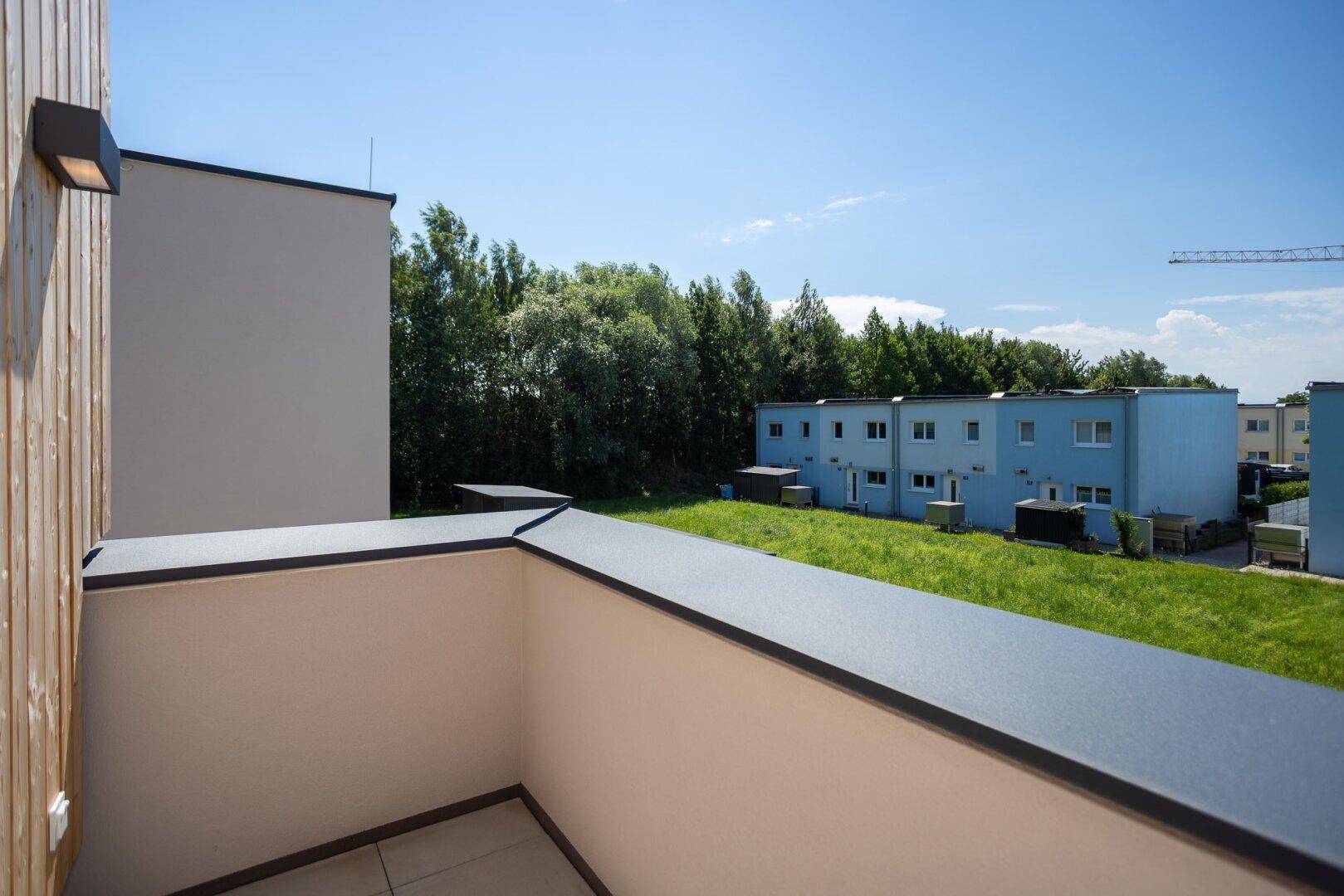 Aussicht vom Balkon auf die grüne Landschaft und die umliegenden Neubauten unter blauem Himmel.