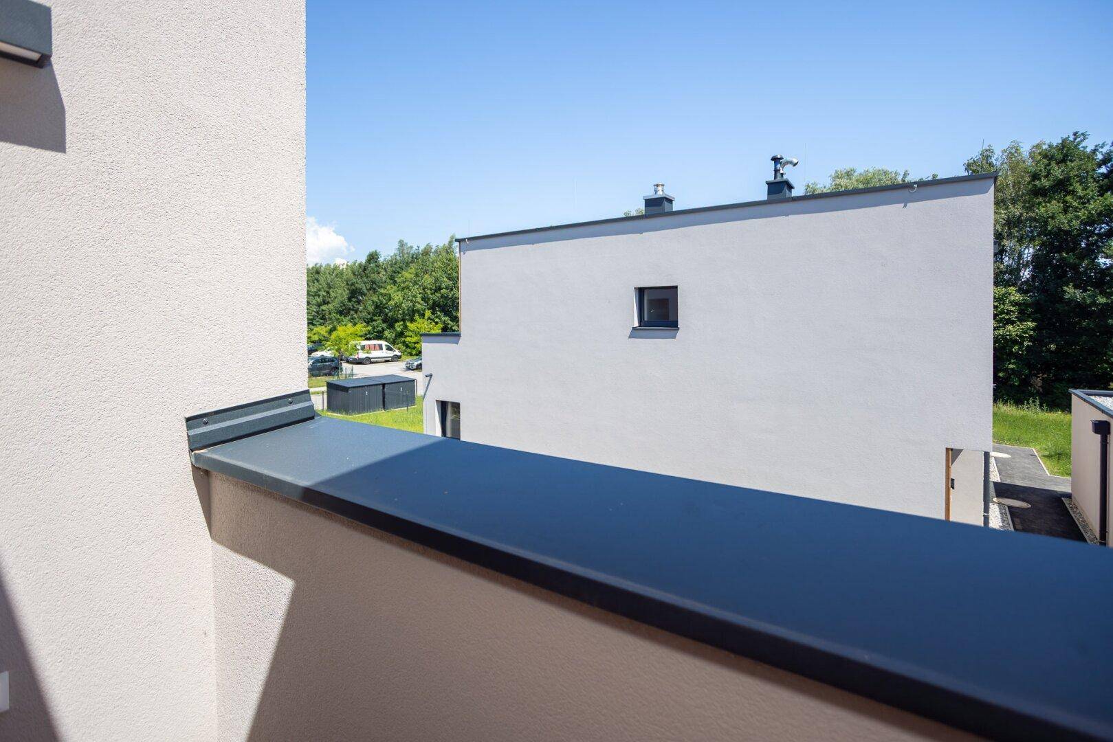 Aussicht vom Balkon auf die moderne Fassade eines Nachbargebäudes und die umgebende Natur.