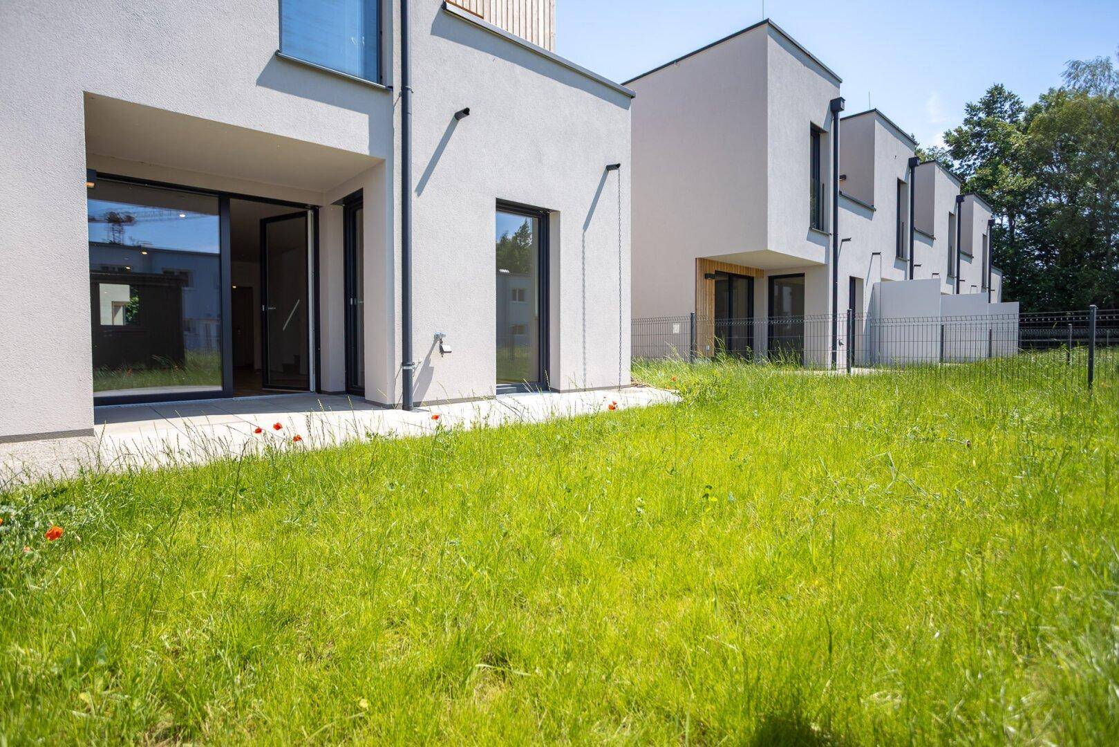 Moderne Reihenhäuser mit weißer Fassade und großen Fenstern, umgeben von einer grünen Rasenfläche.