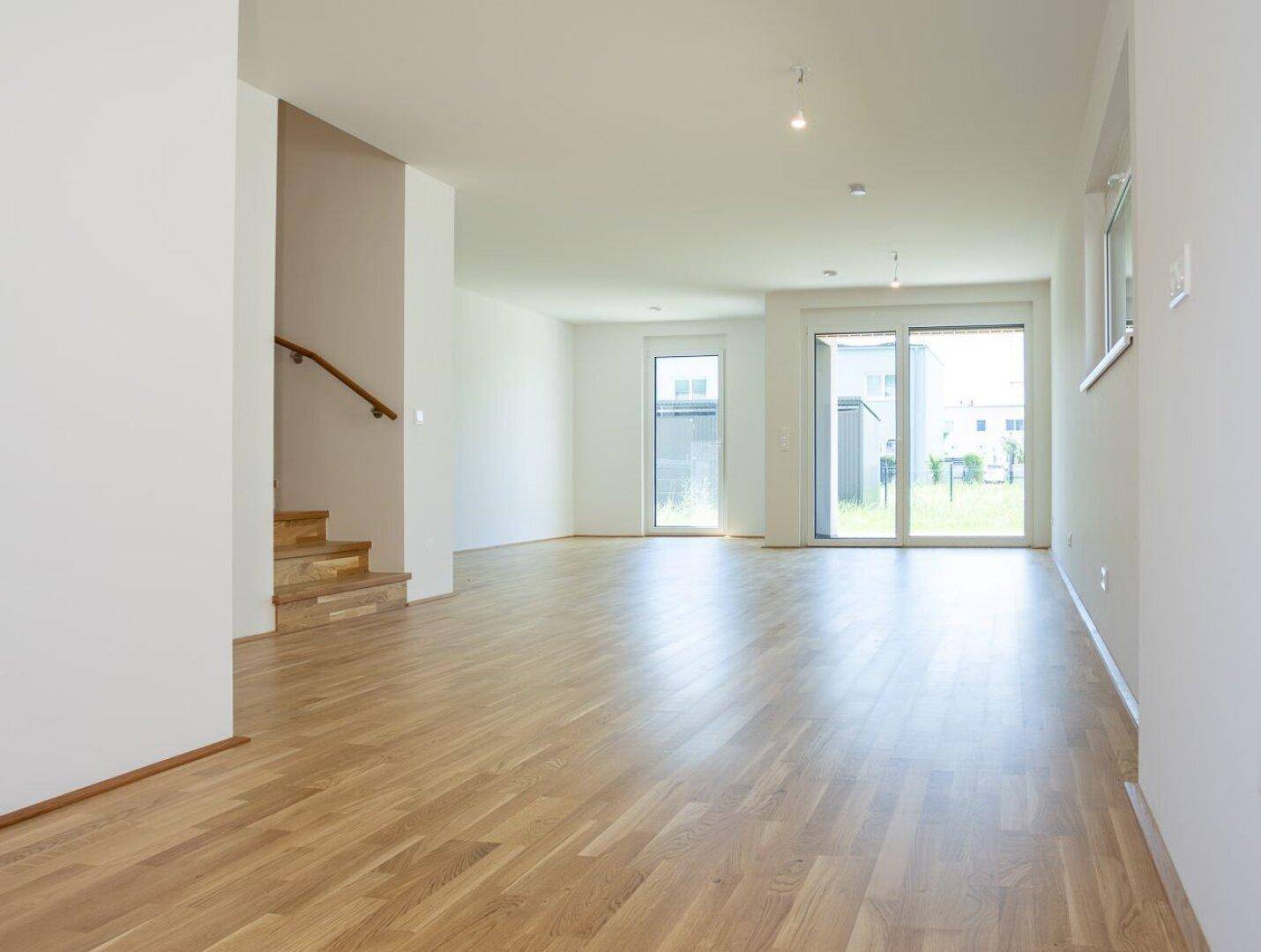 Geräumiger, heller Wohnbereich mit Eichenparkettboden und Zugang zur Terrasse durch große Schiebetüren.