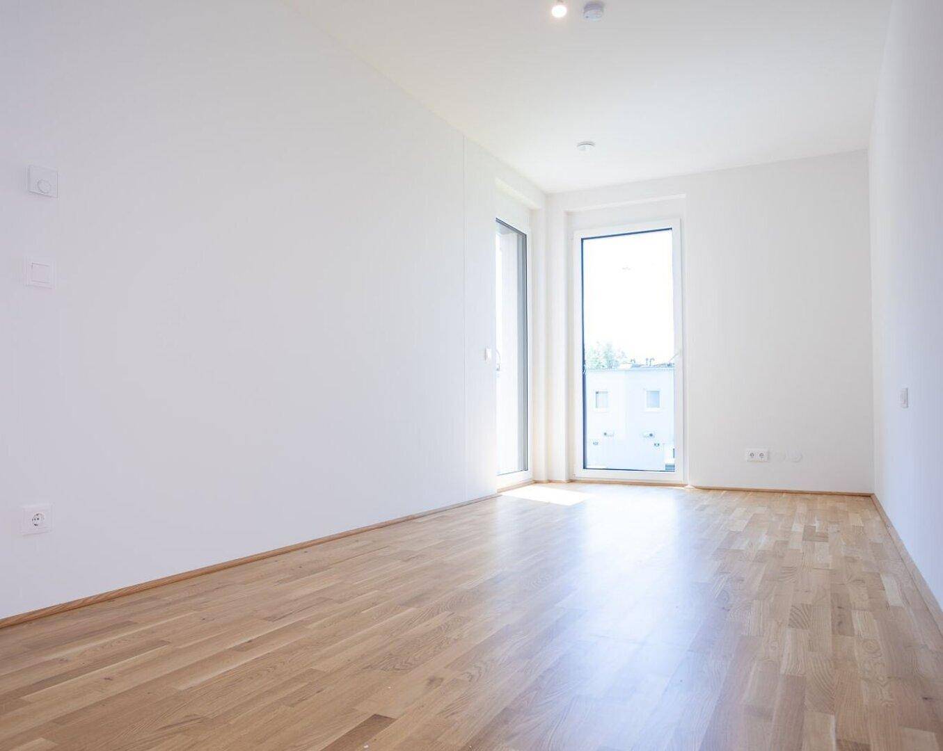 Helles Schlafzimmer mit Eichenparkettboden und Zugang zu einem französischen Balkon, ideal für natürliches Licht.