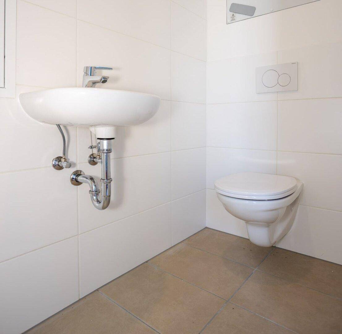 Modernes Gäste-WC mit wandhängendem WC und Waschbecken, komplett gefliest in Weiß.