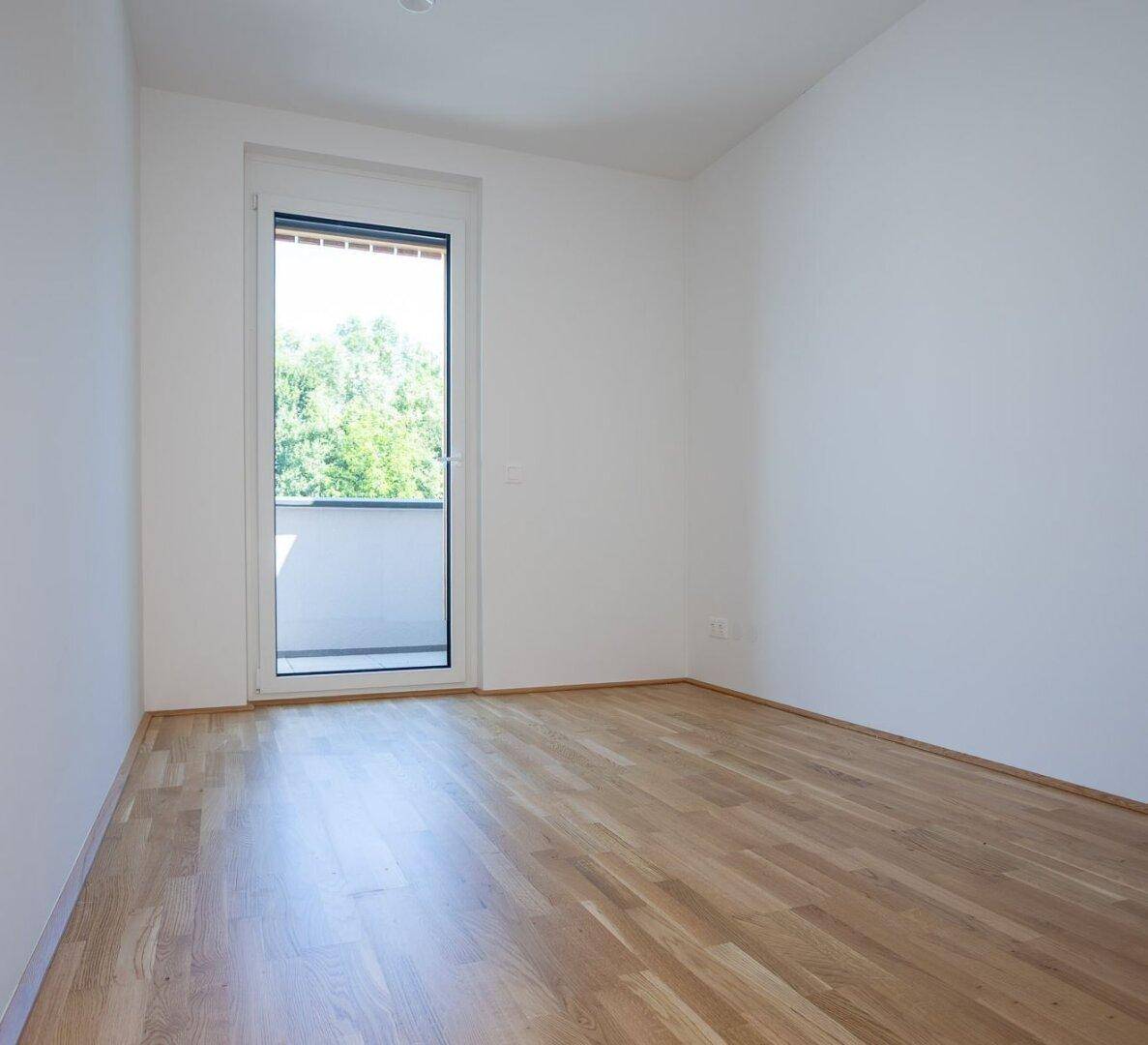Helles Schlafzimmer mit Eichenparkettboden und direktem Zugang zu einem Balkon, bietet viel Tageslicht.