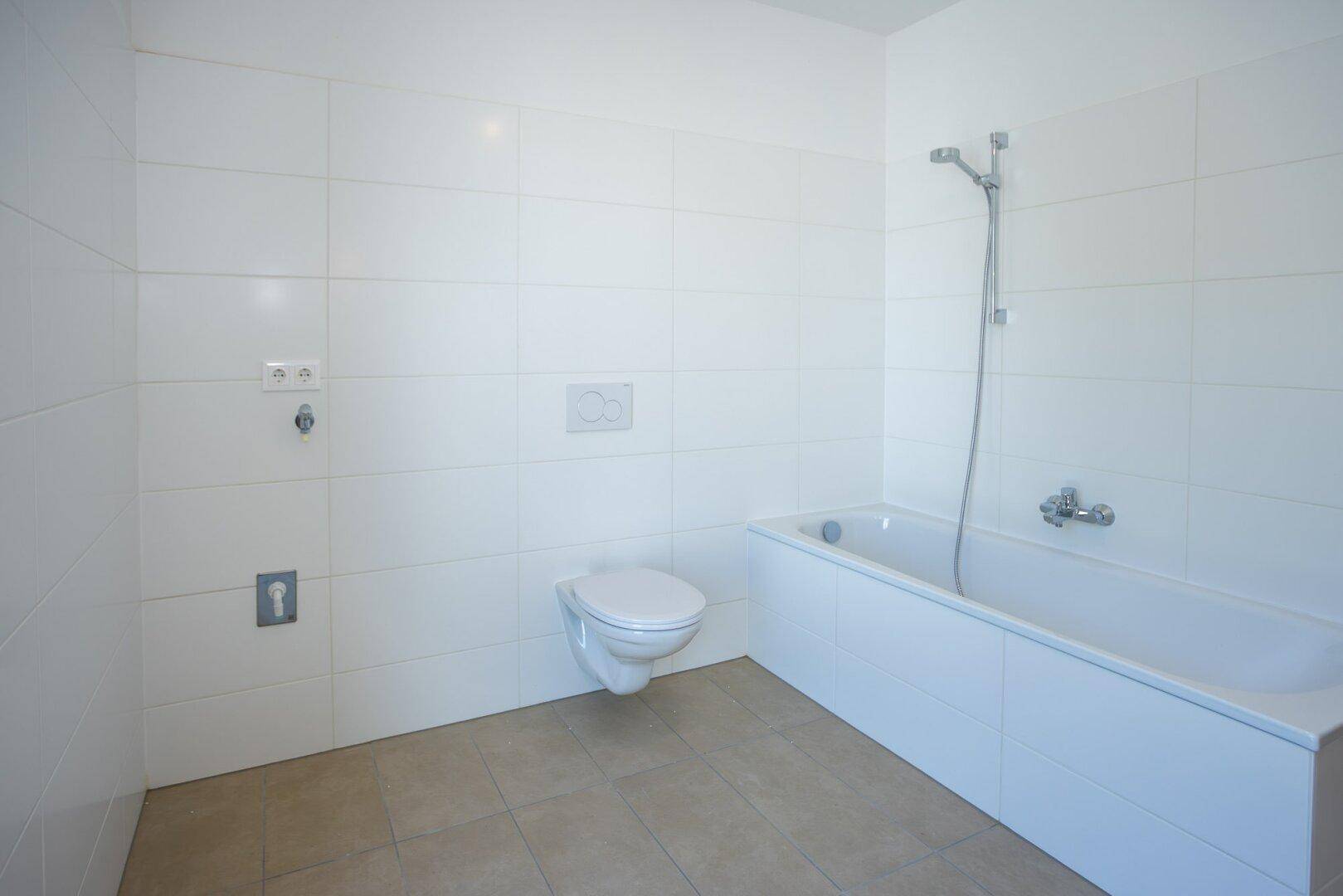Modernes Badezimmer mit weißen Fliesen, Badewanne und wandhängendem WC, bereit zur Nutzung.