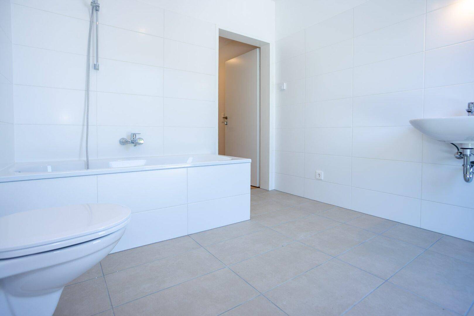 Helles Badezimmer mit weißen Fliesen, Badewanne und wandhängendem WC, bietet eine saubere Ästhetik.
