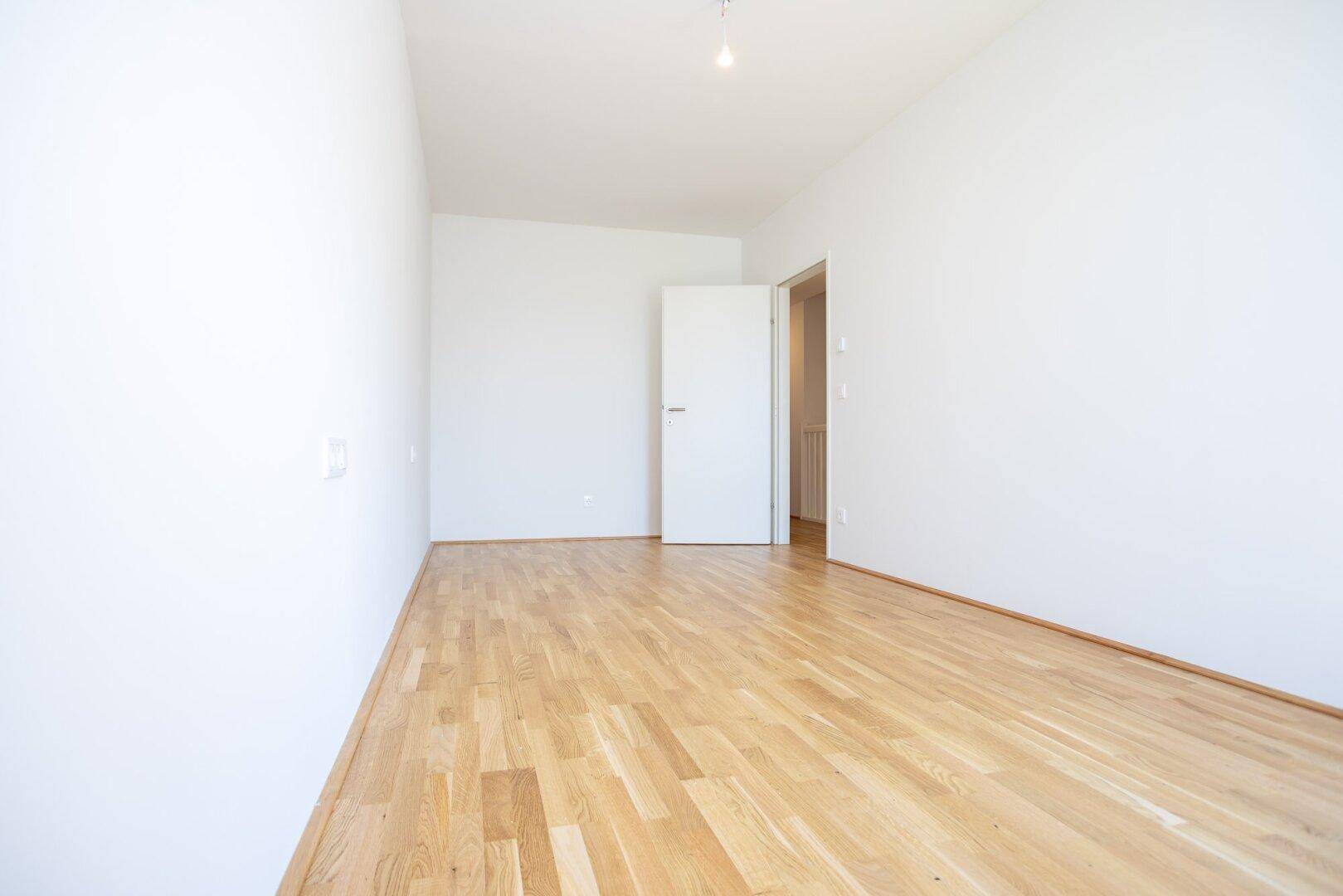 Geräumiges, helles Zimmer mit Eichenparkettboden und weiß gestrichenen Wänden, bereit zur Einrichtung.
