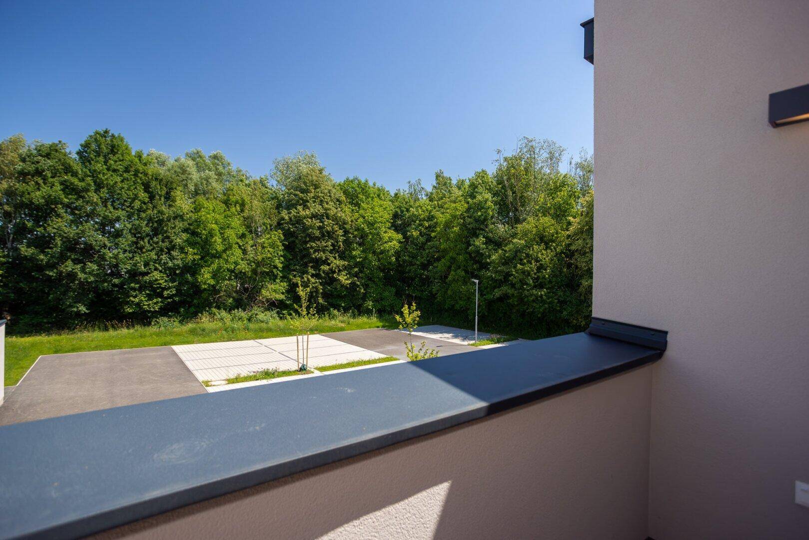 Weitblick vom Balkon über eine Parkfläche und die angrenzende grüne Waldlandschaft.