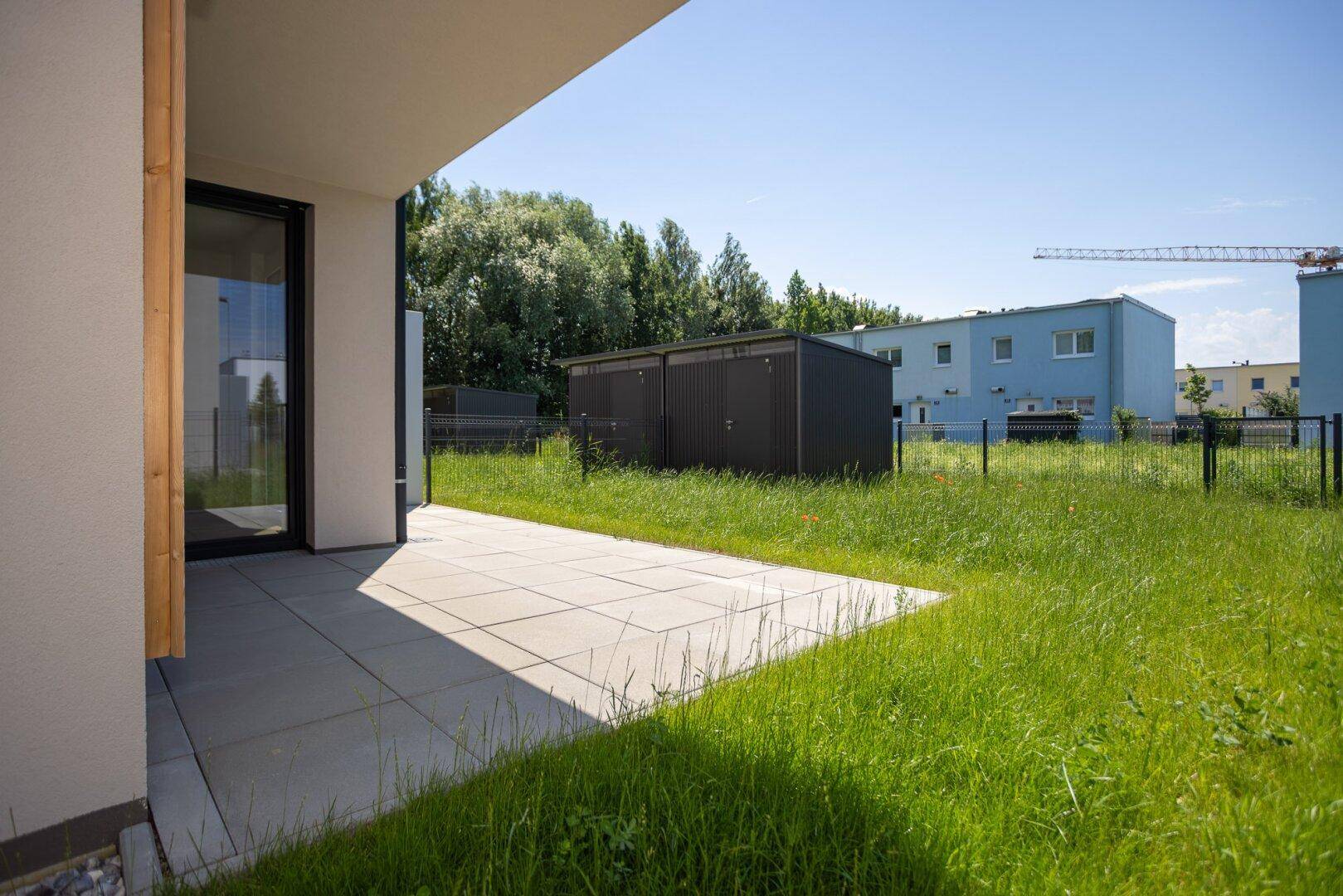 Sonniger Terrassenbereich mit hellen Fliesen und Blick auf die grüne Rasenfläche und die Umgebung.