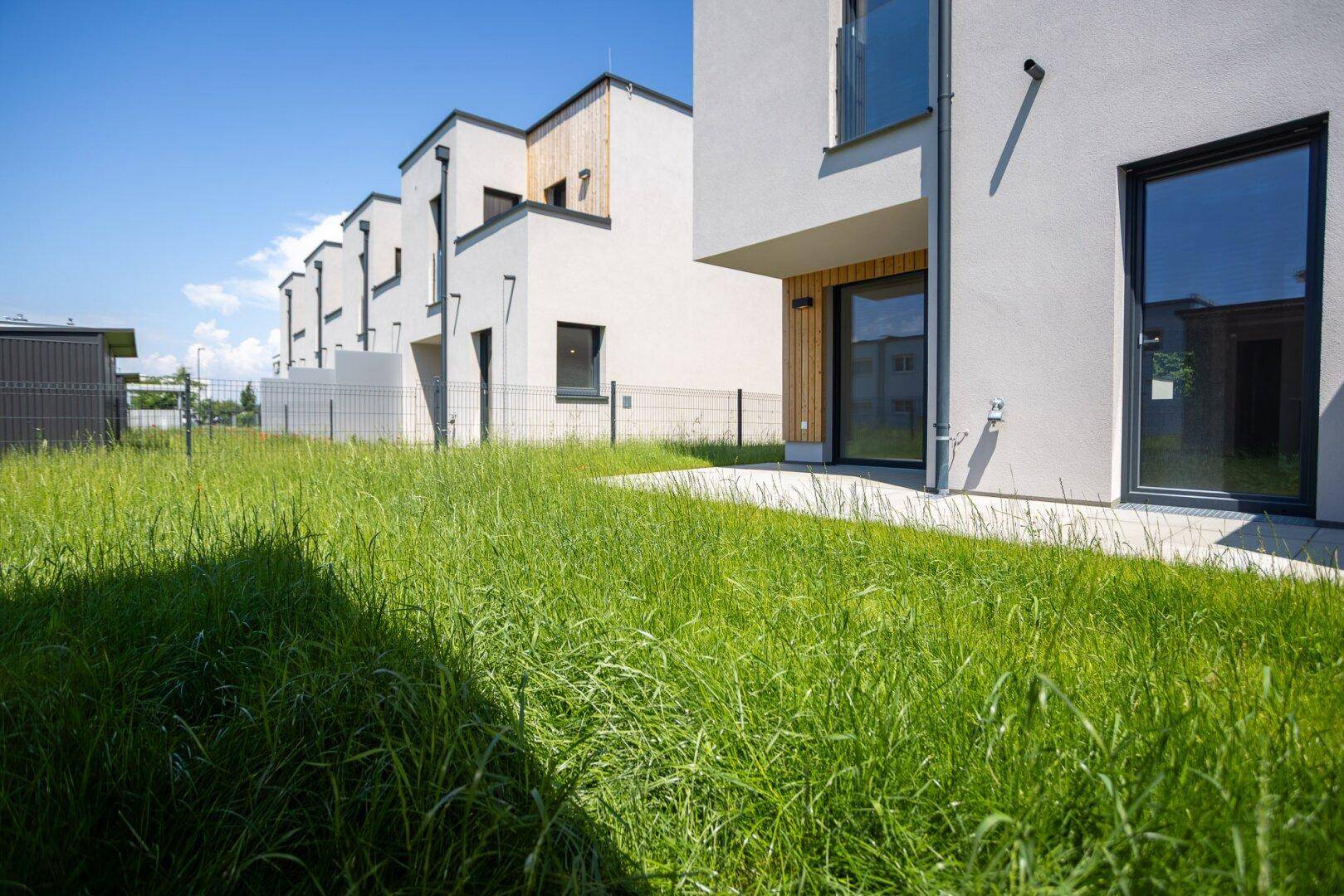 Weitläufige Rasenfläche hinter den modernen Reihenhäusern, ideal für Erholung im Freien.