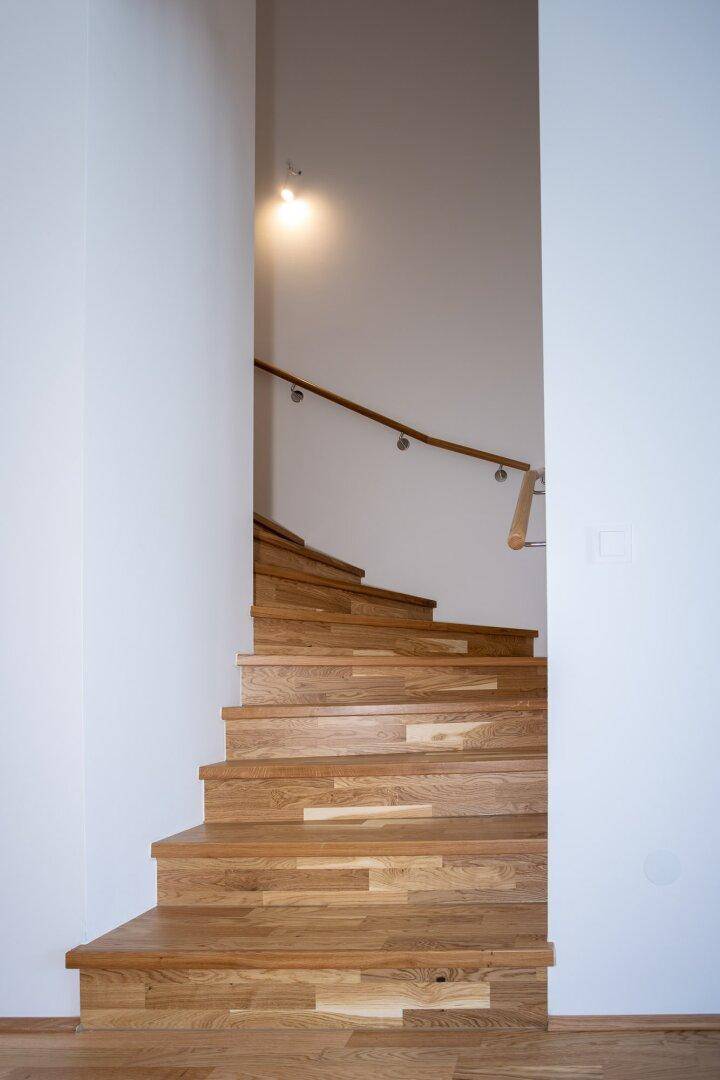 Elegante Holztreppe mit Handlauf, die in die obere Etage führt, in einem hellen Treppenhaus.