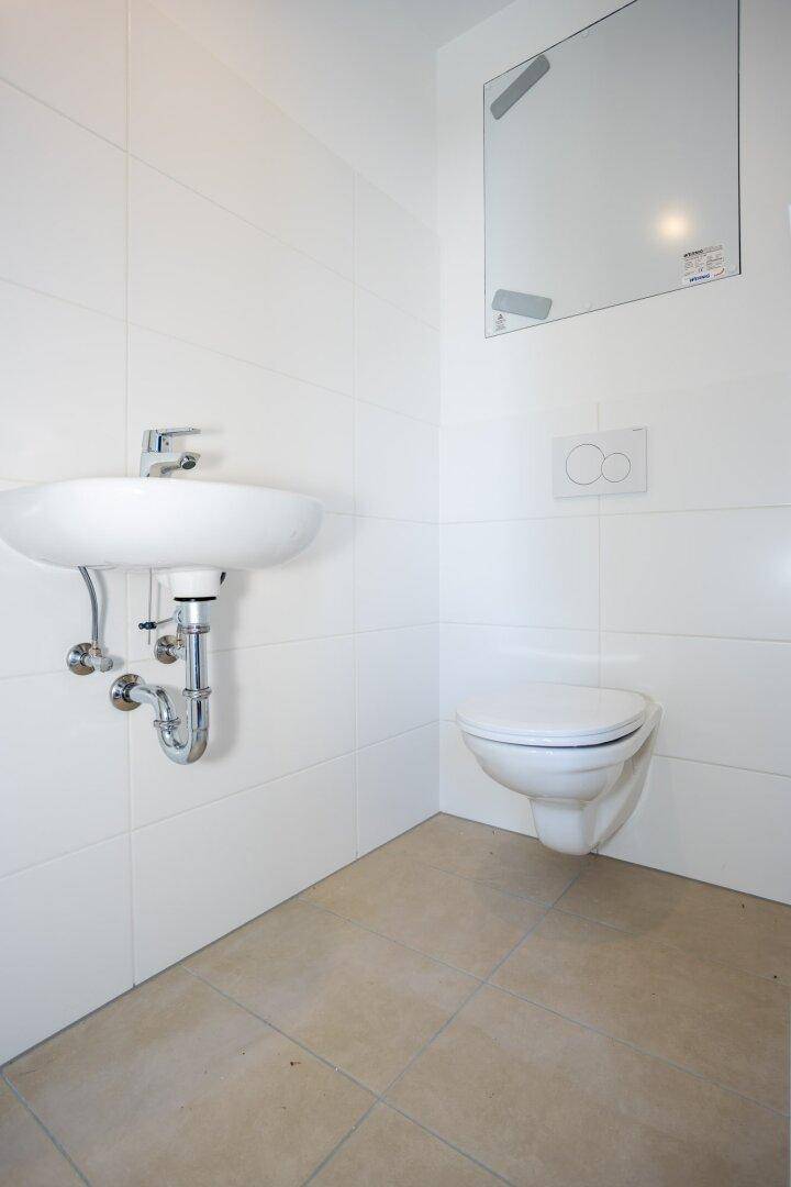 Modernes Gäste-WC mit wandhängender Toilette, kleinem Waschbecken und Spiegel.