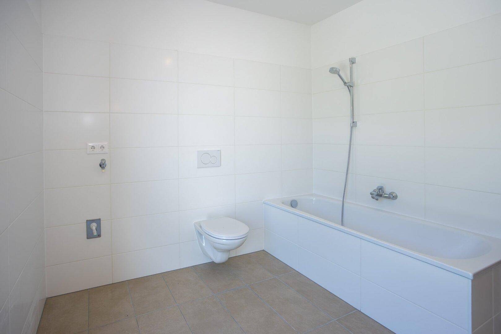 Helles Badezimmer mit weißen Wandfliesen, einer Badewanne und einer wandhängenden Toilette.
