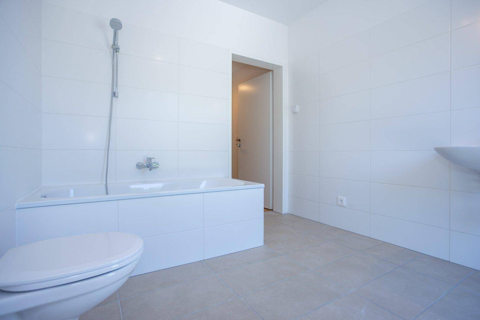 Sauberes Badezimmer mit Badewanne, Toilette und weißen Fliesen, bereit für die erste Nutzung.