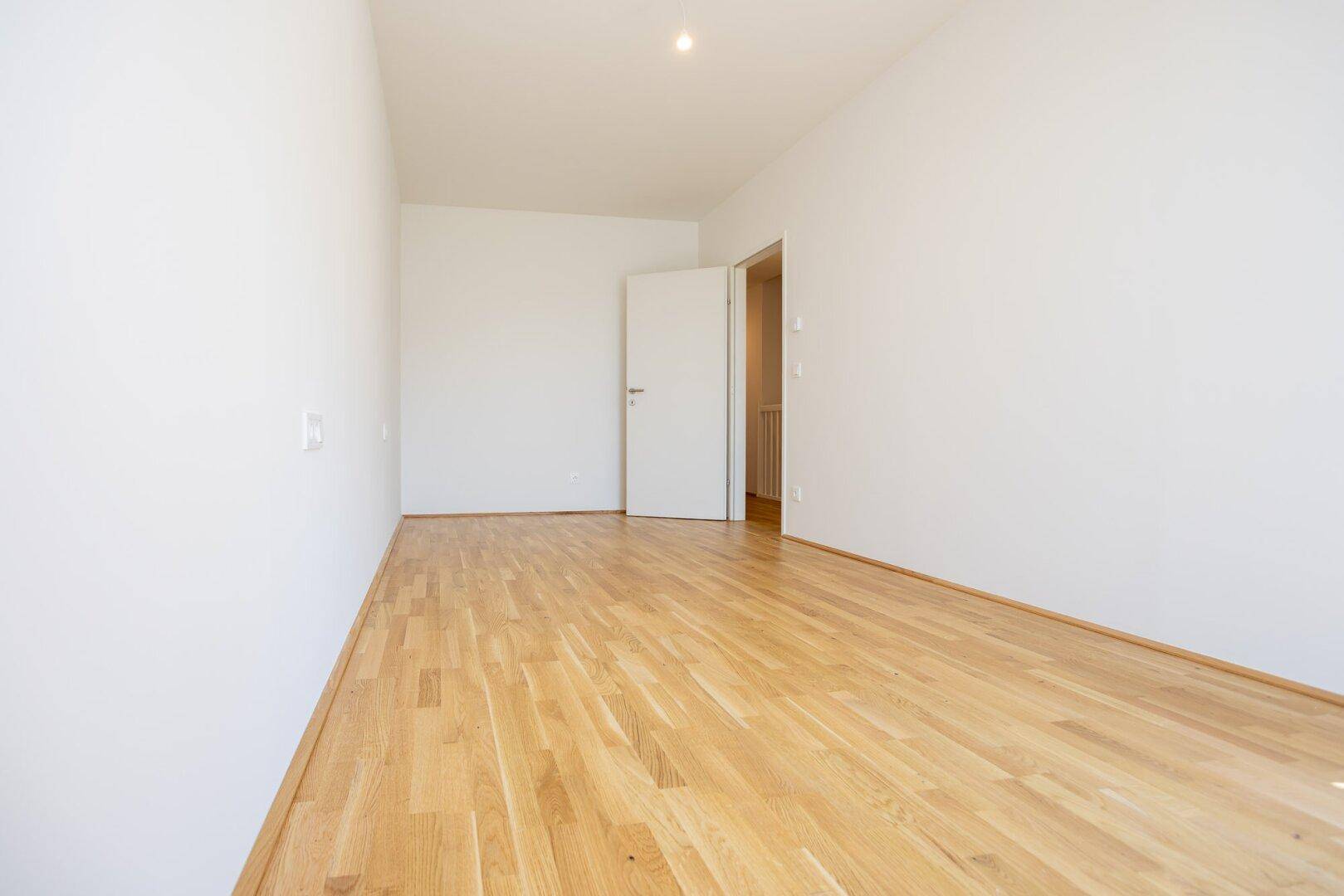 Leeres Schlafzimmer mit hellem Parkettboden und weißen Wänden, bereit zur individuellen Gestaltung.