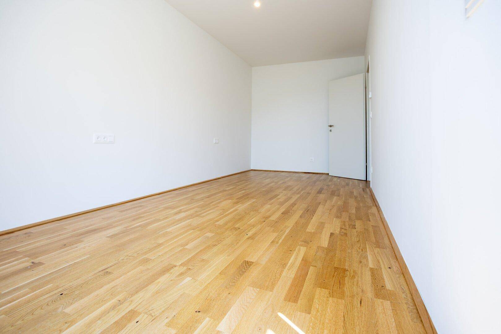 Geräumiges, leeres Zimmer mit Parkettboden und weißen Wänden, ideal als Schlaf- oder Arbeitszimmer.