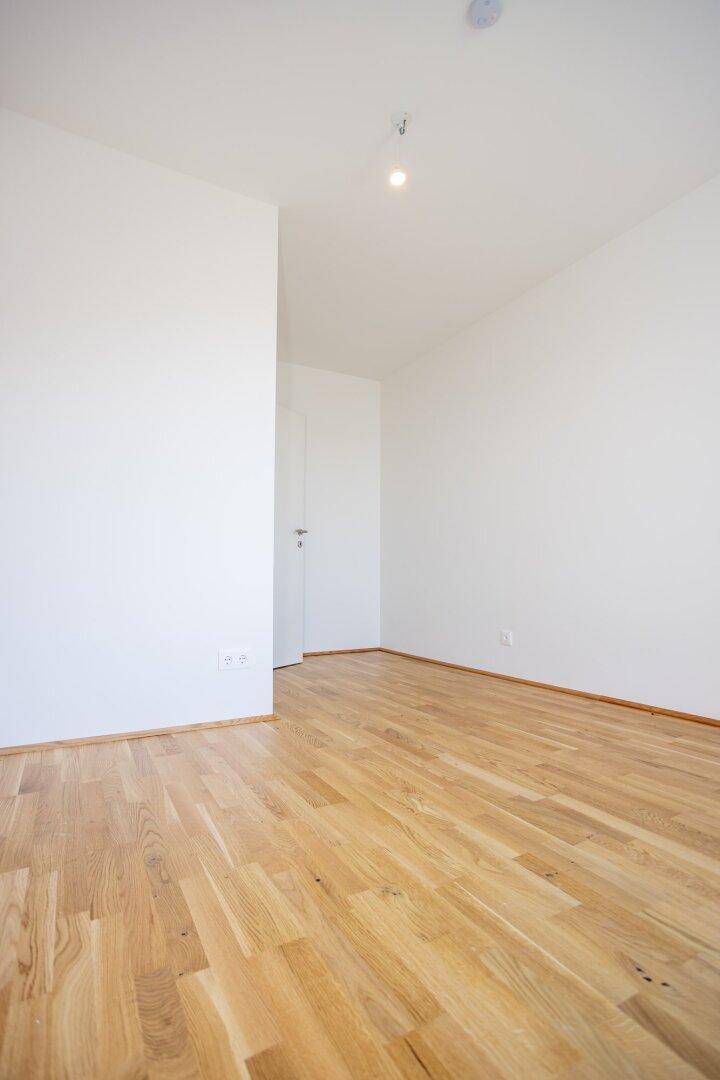 Helles, leeres Zimmer mit Parkettboden und weiß gestrichenen Wänden, ideal für individuelle Einrichtung.