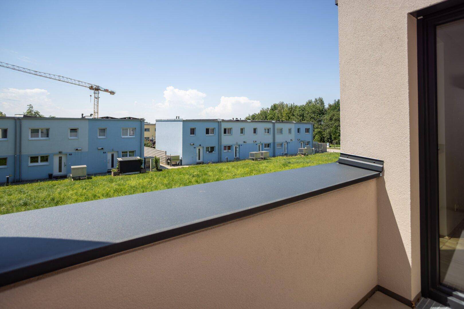 Balkon mit Blick auf eine grüne Umgebung und weitere moderne Reihenhäuser in der Ferne.