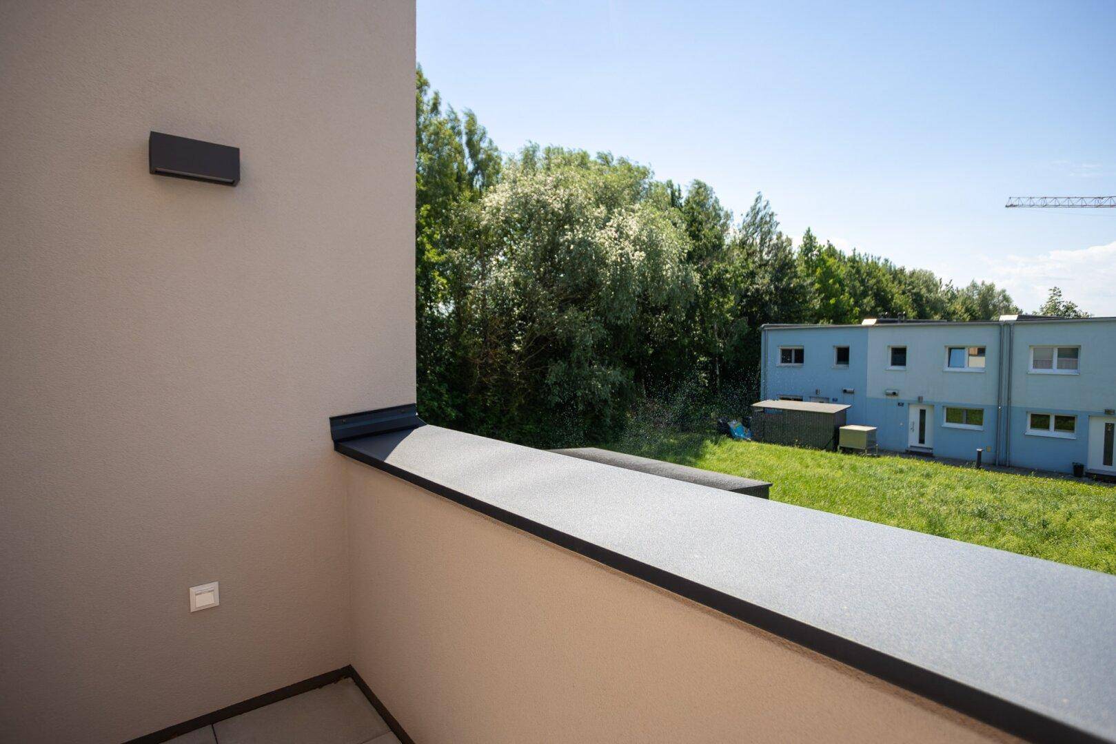 Kleiner Balkon mit seitlichem Blick auf Bäume und eine ruhige, grüne Umgebung.