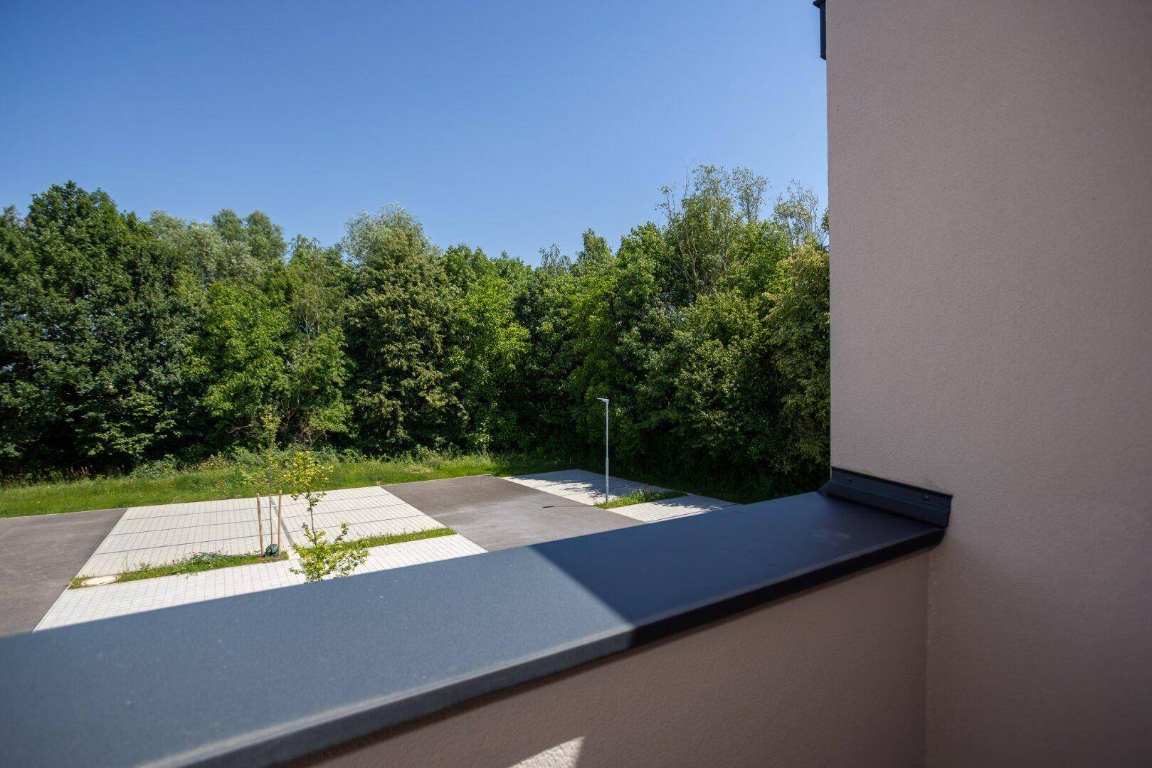 Balkon mit weitem Blick auf eine grüne Landschaft und einen Parkplatz im Vordergrund.