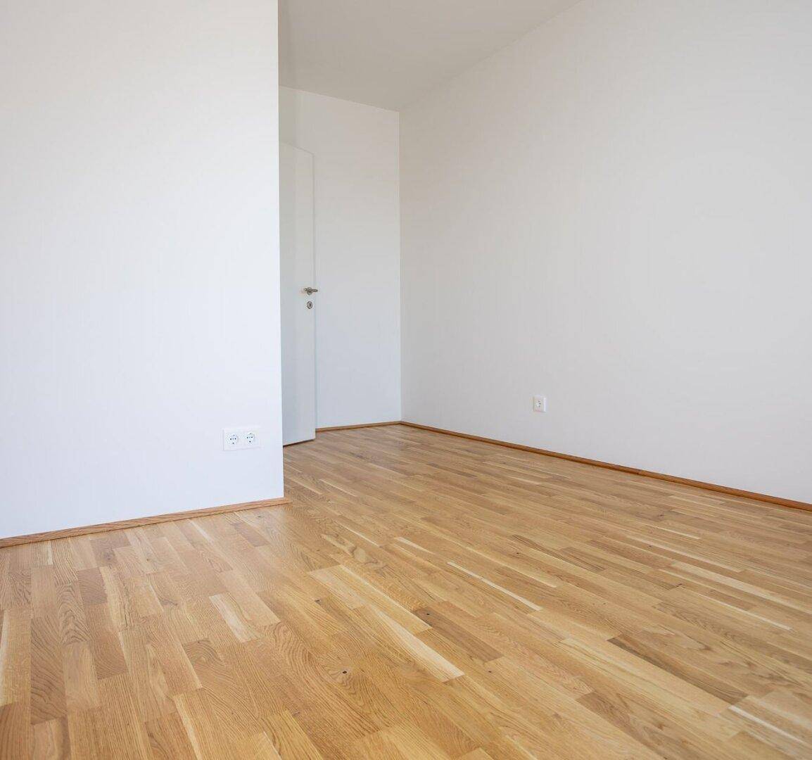 Helles Zimmer mit Eichenparkettboden und schlichten weißen Wänden.